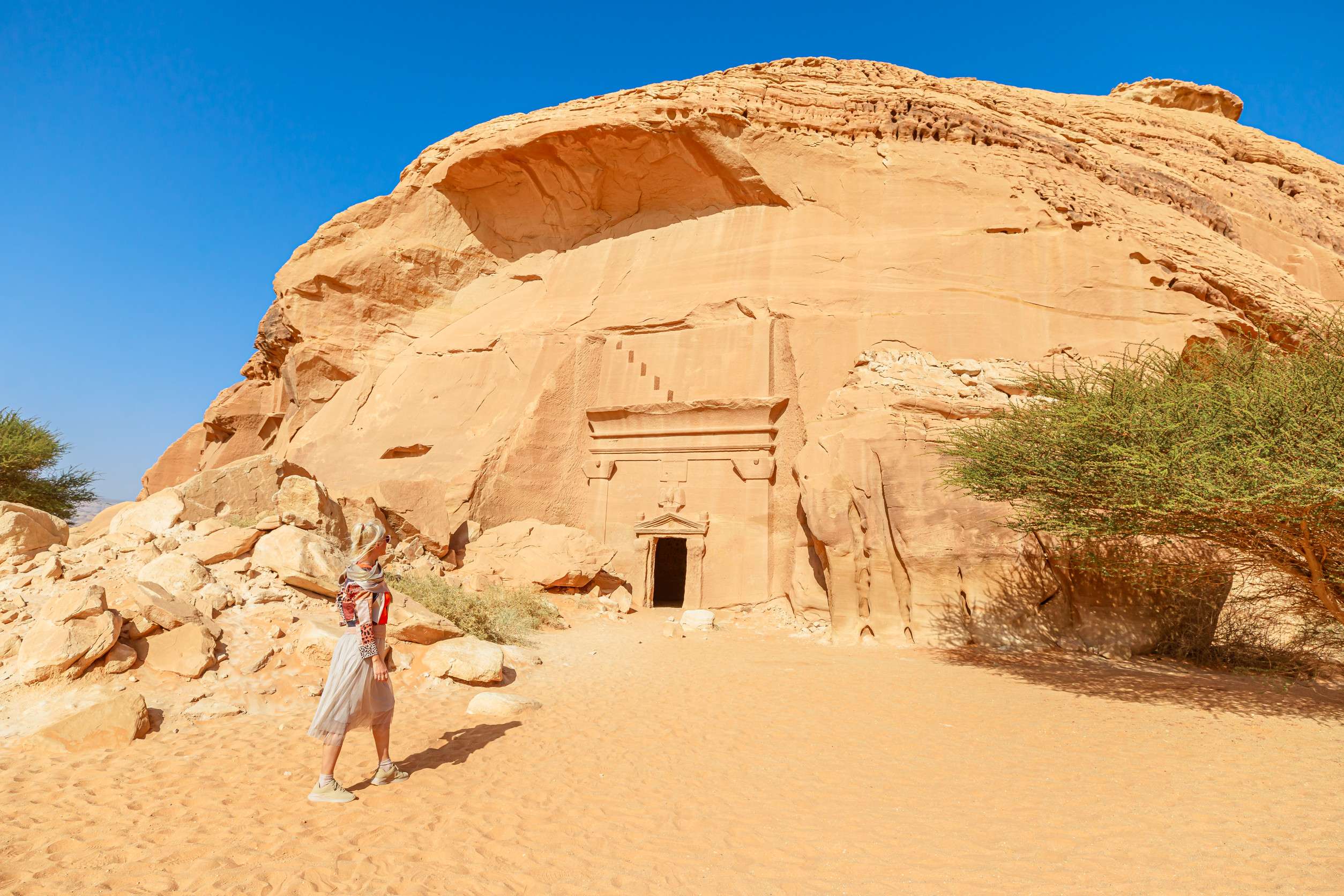 Blonde Tourist Walking In The Desert Next To Of Jabal Albanat And Giant Rock Cut Tomb Of The Blonde Tourist Walking In The Desert Next To Of Jabal Albanat And Giant Rock Cut Tomb Of The