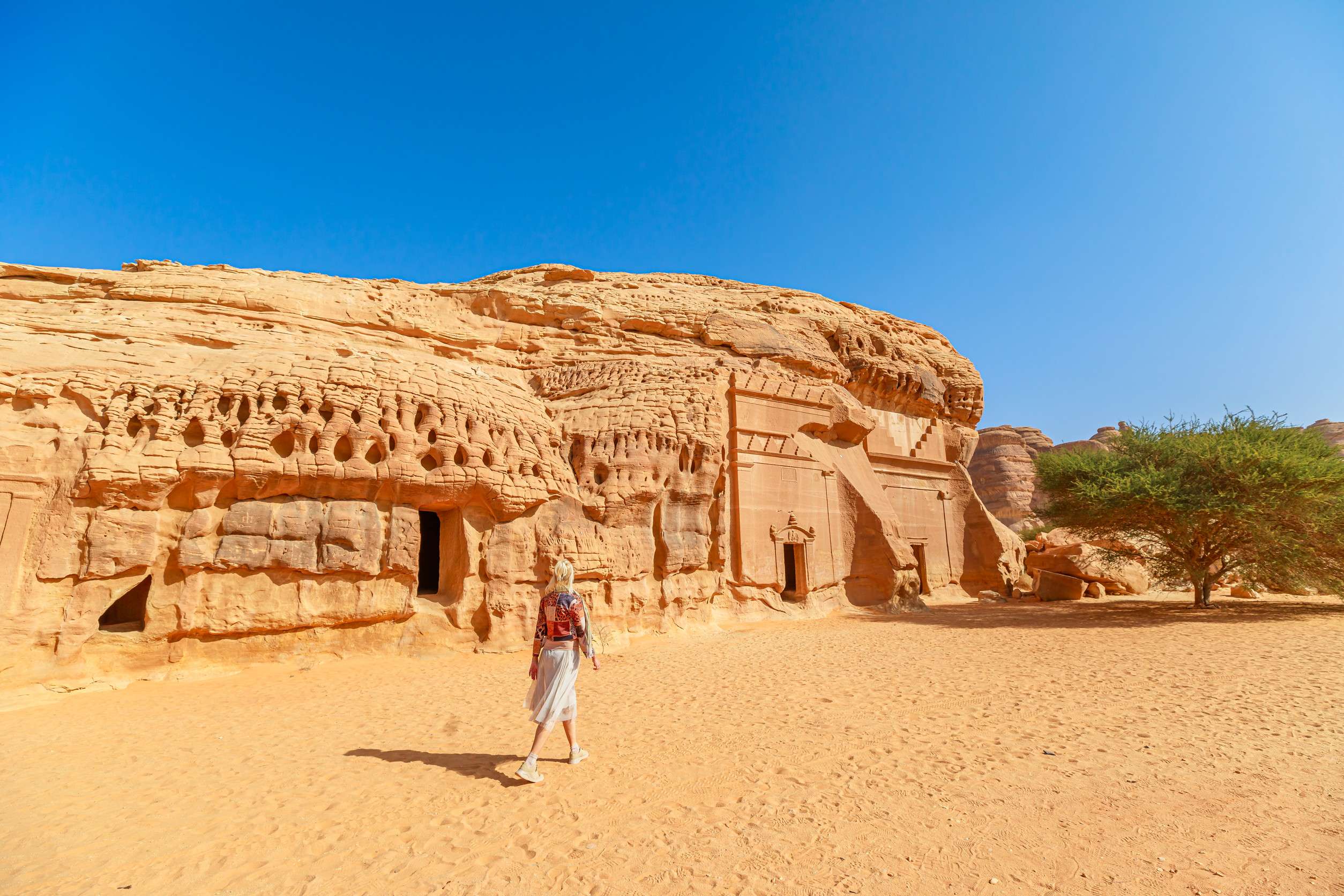 Blonde Tourist Walking In The Desert Next To Of Jabal Albanat And Giant Rock Cut Tomb Of The Blonde Tourist Walking In The Desert Next To Of Jabal Albanat And Giant Rock Cut Tomb Of The