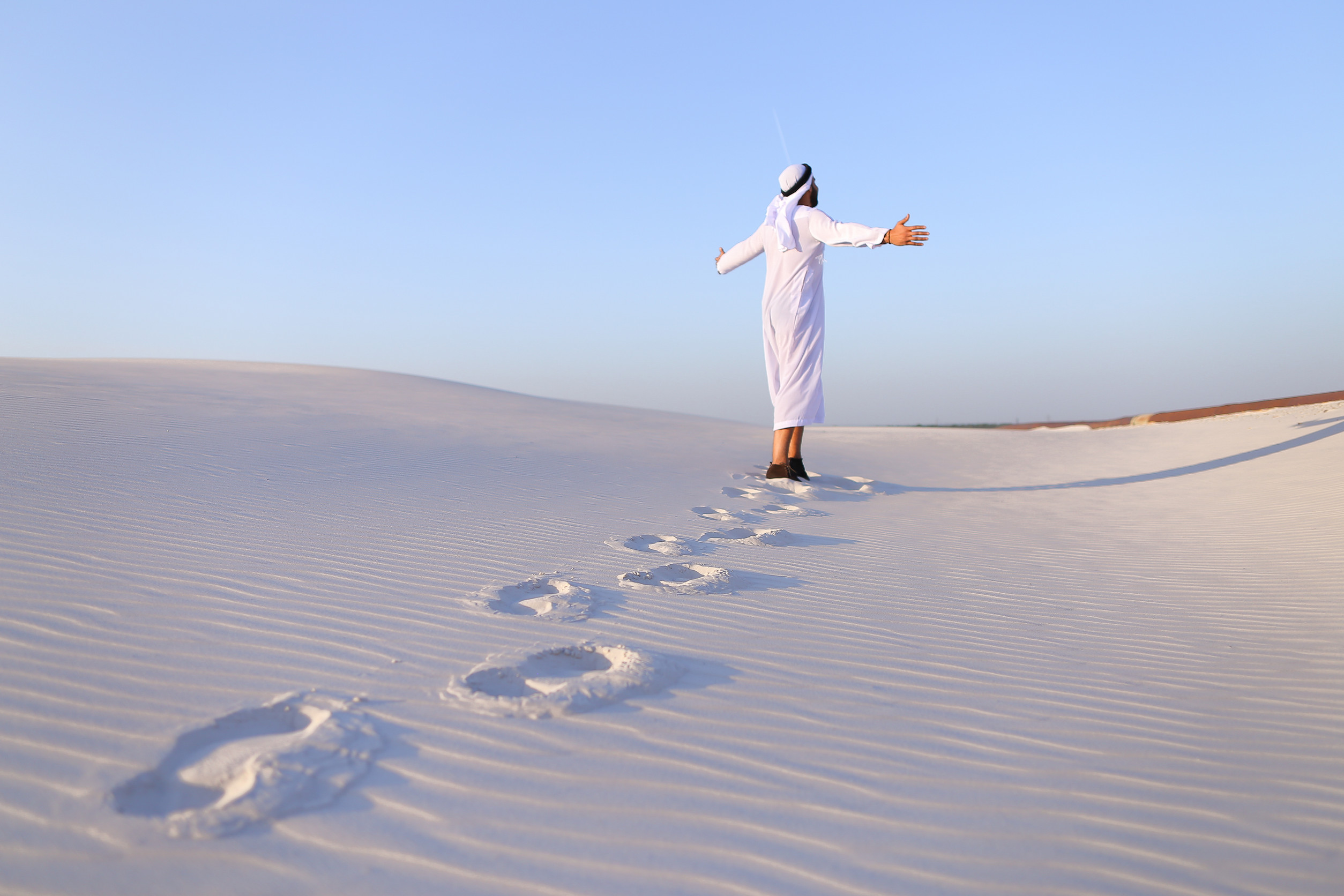 Confident Arabian Tourist Guy Walks On Foot Along Expanses Of White Sand Desert Leaving Traces Confident Arabian Tourist Guy Walks On Foot Along Expanses Of White Sand Desert Leaving Traces