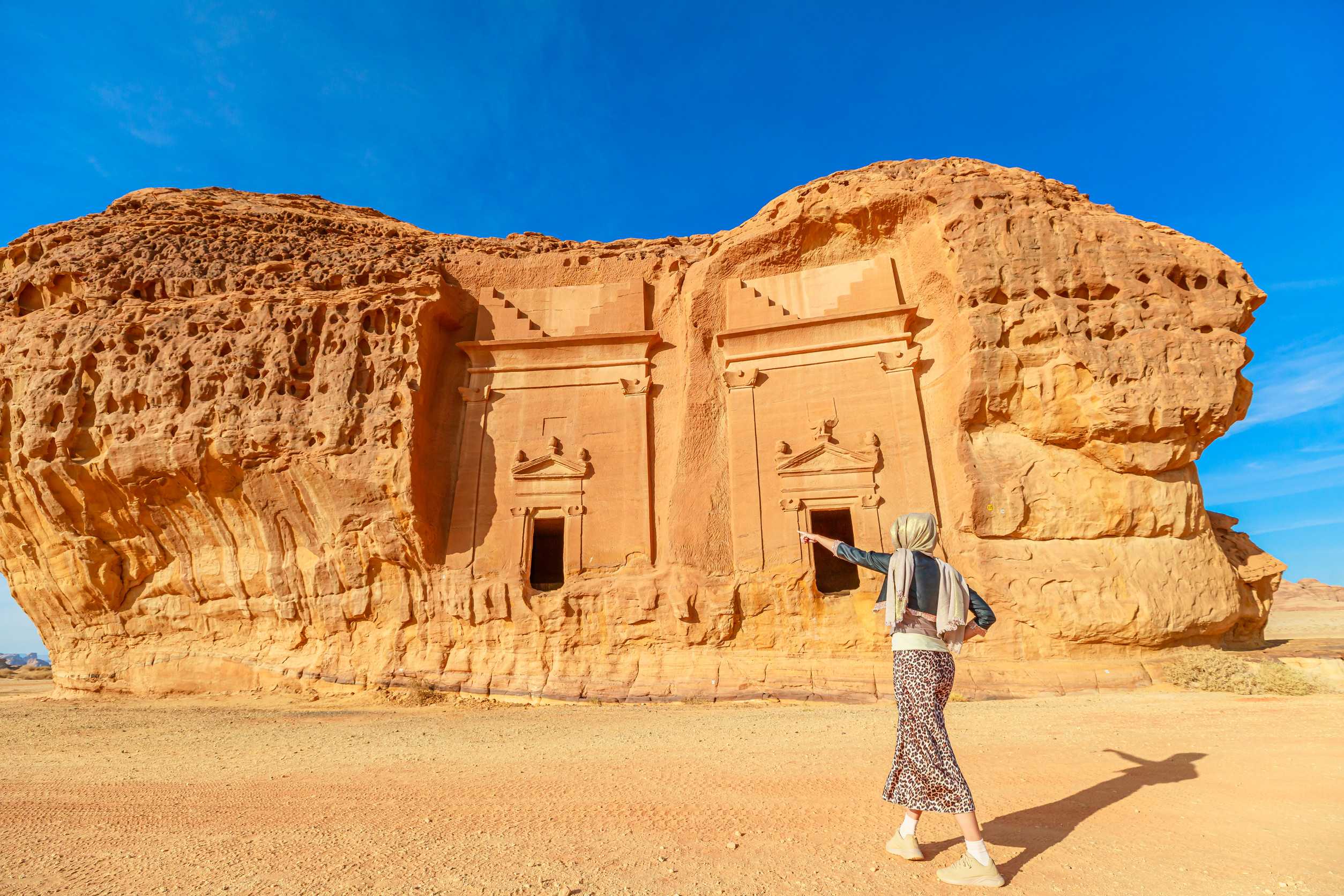 Tourist Pointing At Ancient Nabataean Rock Cut Tombs Of Jabal Al Ahmar In Hegra Archaeological Si Tourist Pointing At Ancient Nabataean Rock Cut Tombs Of Jabal Al Ahmar In Hegra Archaeological Si